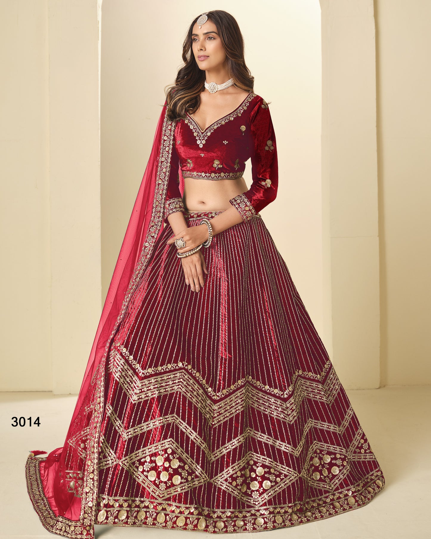 Woman wearing a red and maroon embroidered traditional outfit on a beige background