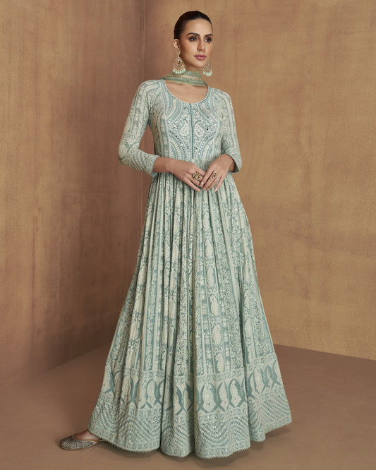 Woman wearing a light green traditional dress with intricate patterns against a brown background