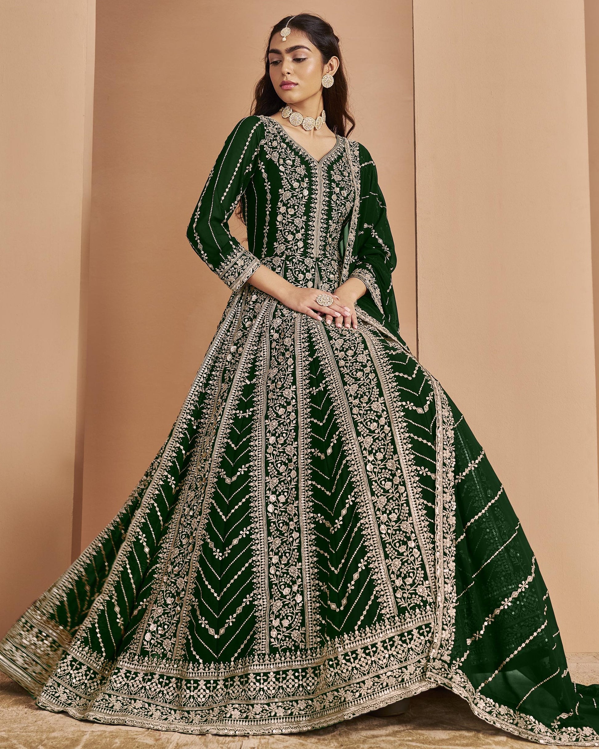 Woman wearing a green and silver embroidered traditional outfit against a beige background