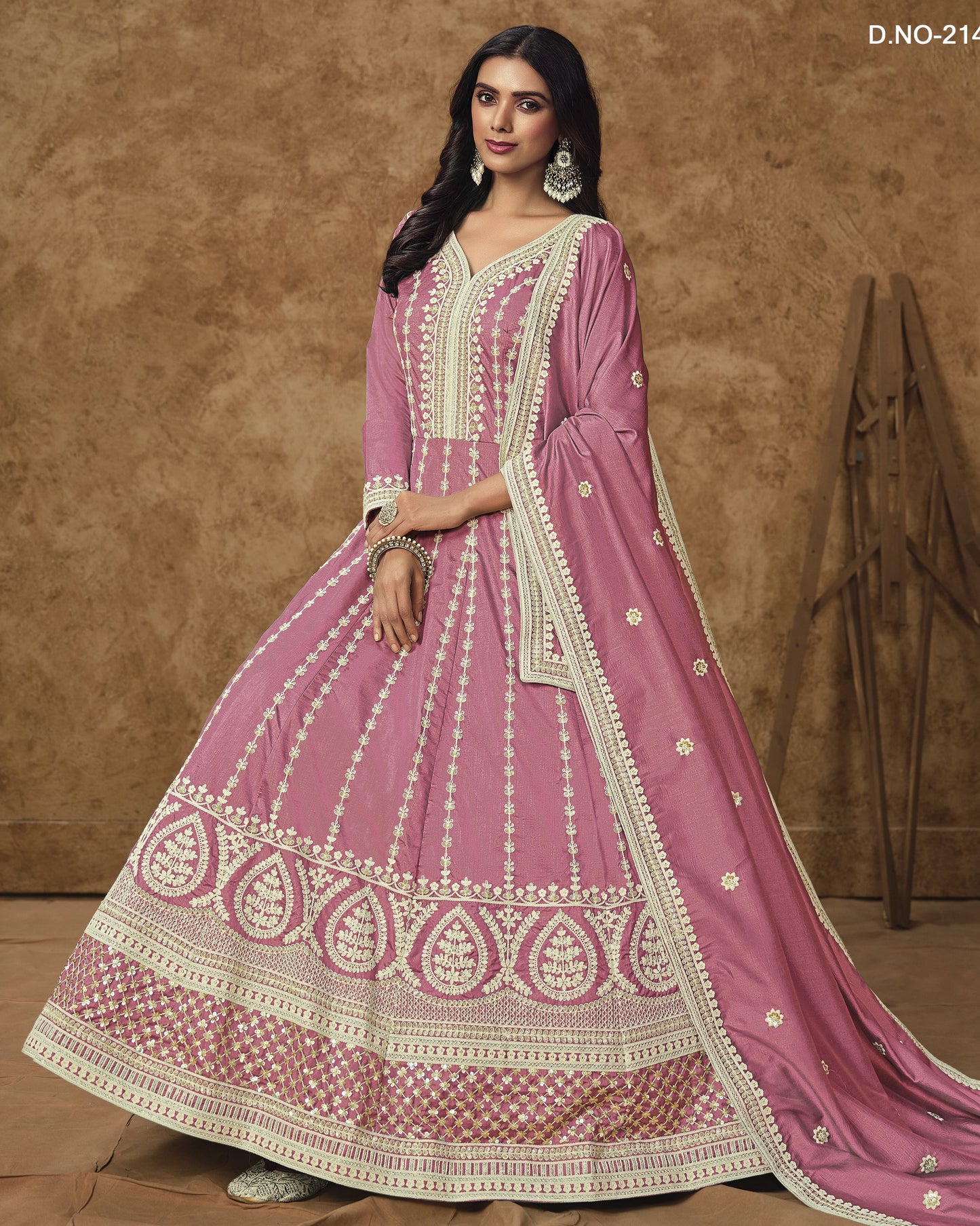 Woman wearing a pink traditional outfit with white embroidery against a brown background