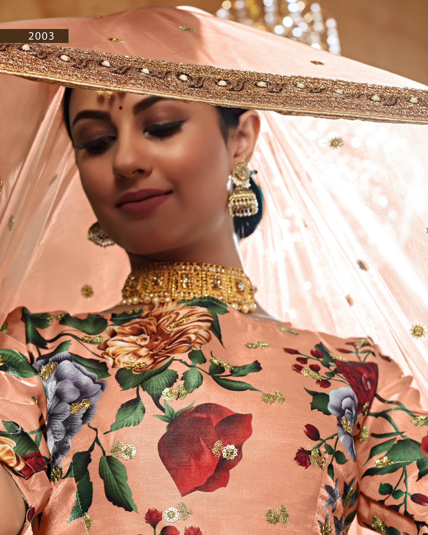 Woman wearing a traditional outfit with floral patterns and gold jewelry, holding a decorative pink umbrella.