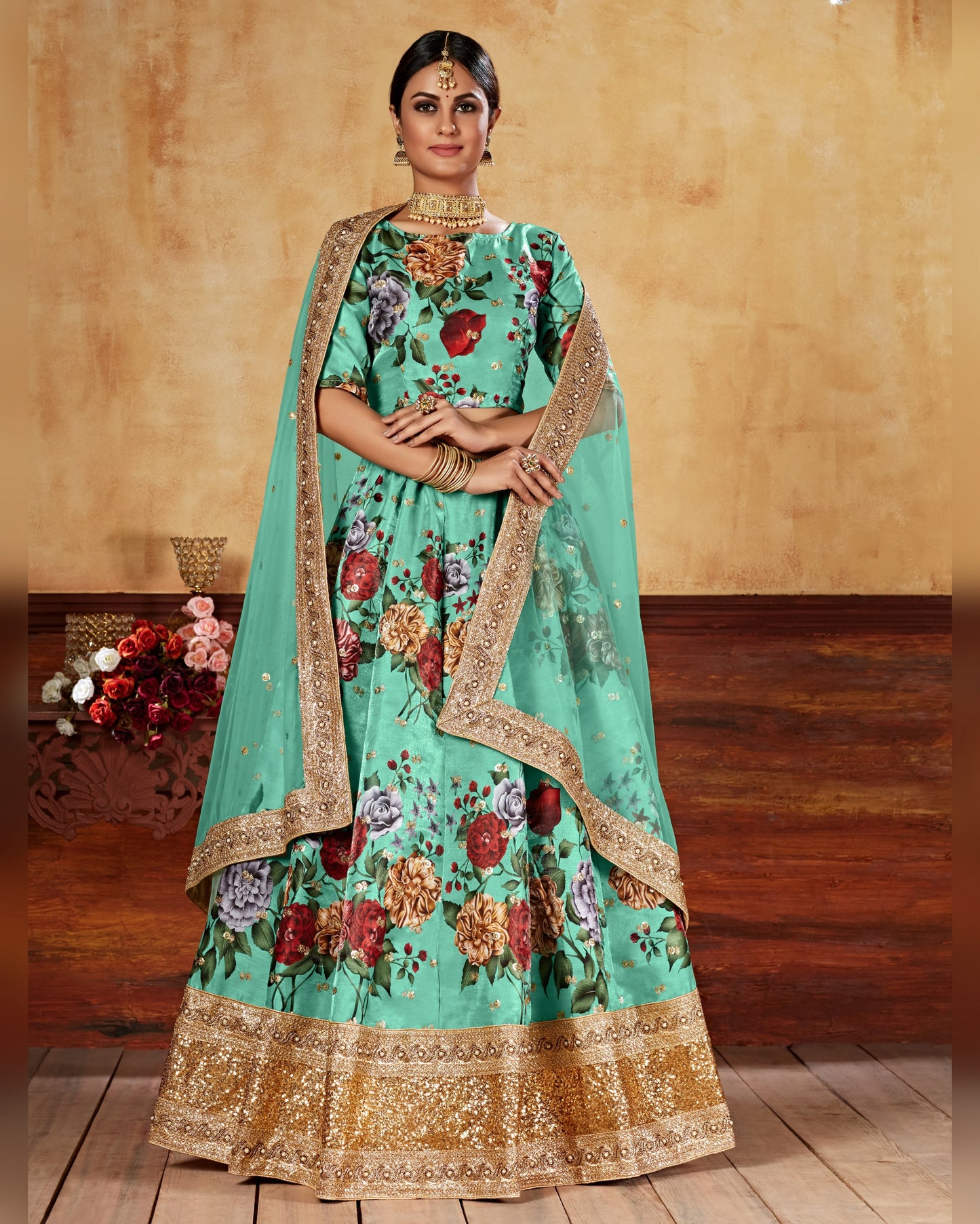 Woman wearing a traditional turquoise embroidered outfit with gold details on a wooden floor.