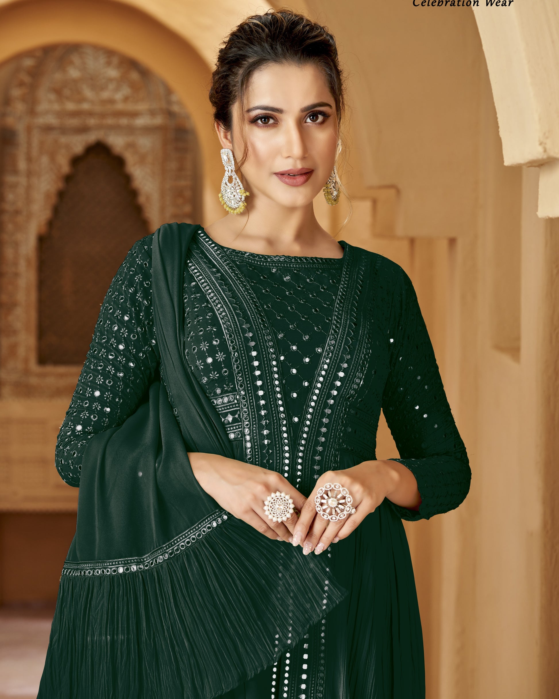 Woman in a dark green traditional outfit with jewelry against an architectural background