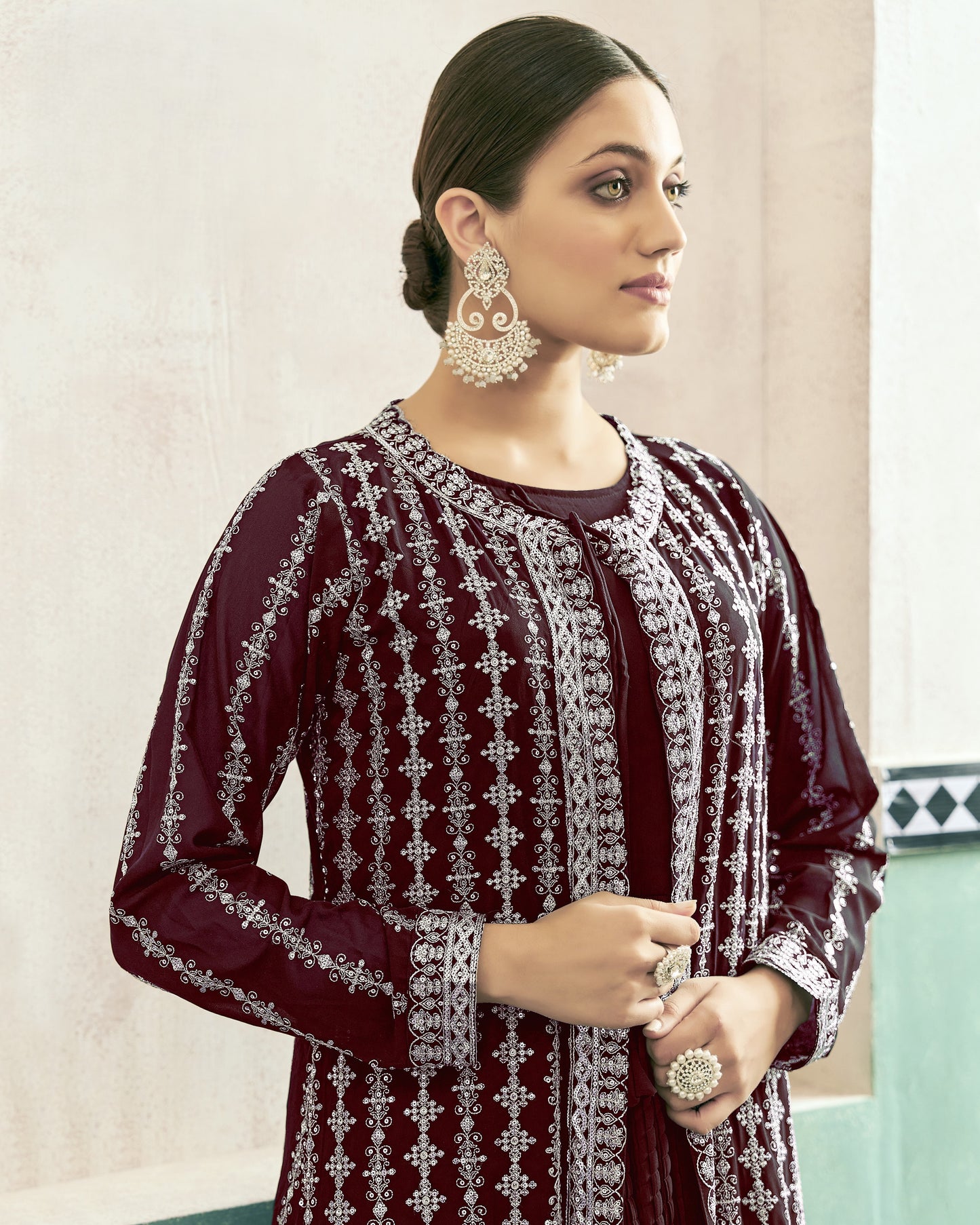 Woman wearing a maroon embroidered outfit with silver details against a light background