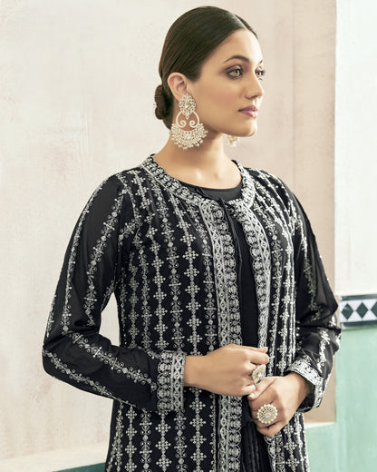 Woman wearing a black and silver embroidered outfit with earrings and rings indoors.