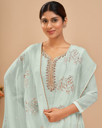 Woman wearing a light blue embroidered traditional outfit against a beige background