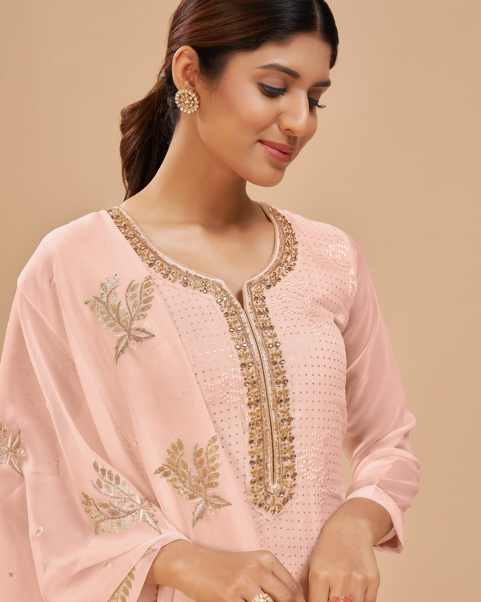 Woman wearing a light pink embroidered traditional outfit on a beige background