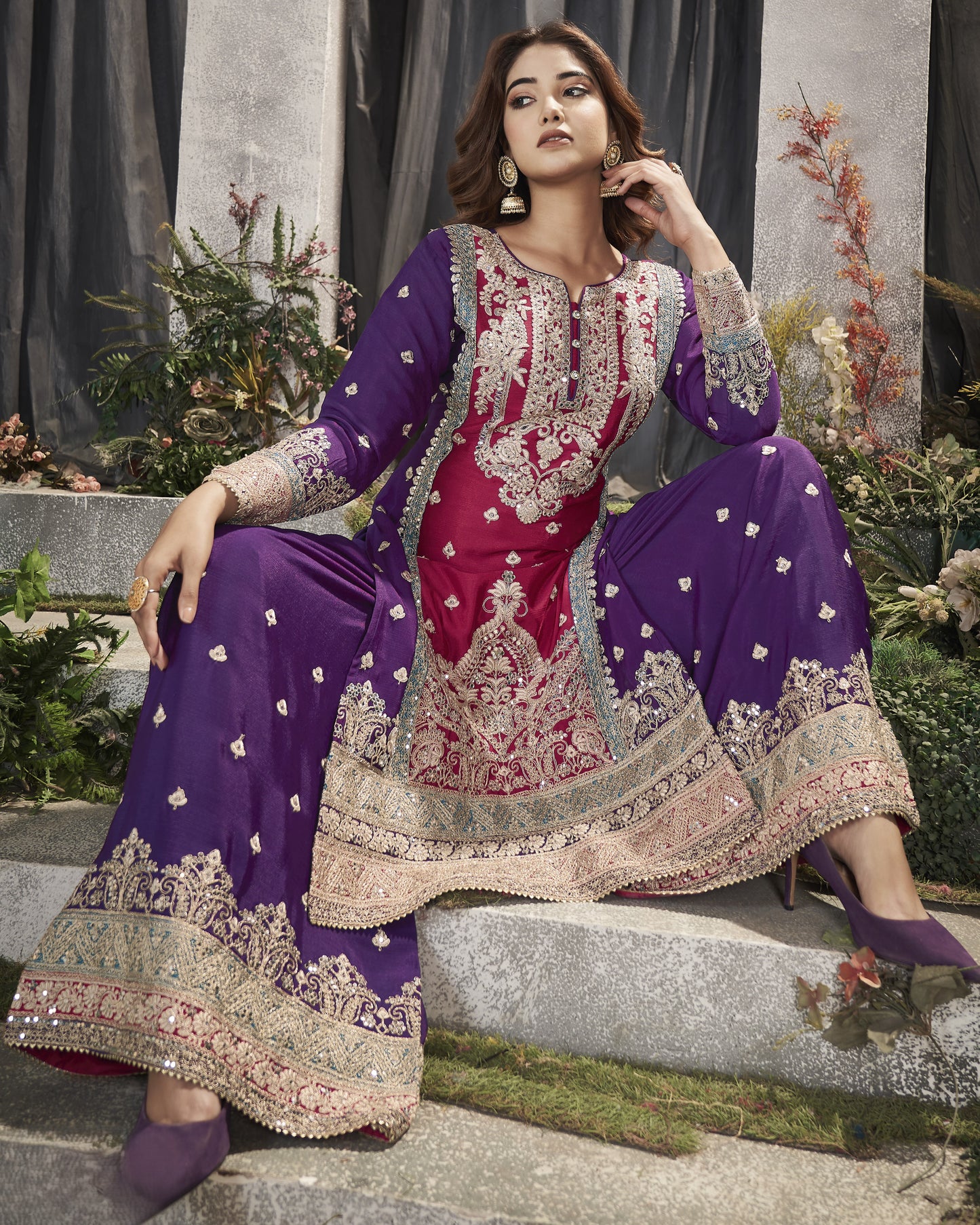 Woman in a traditional embroidered outfit with purple and pink colors, sitting outdoors.