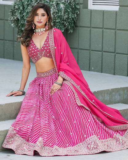 Woman in a pink traditional outfit sitting on steps with greenery in the background
