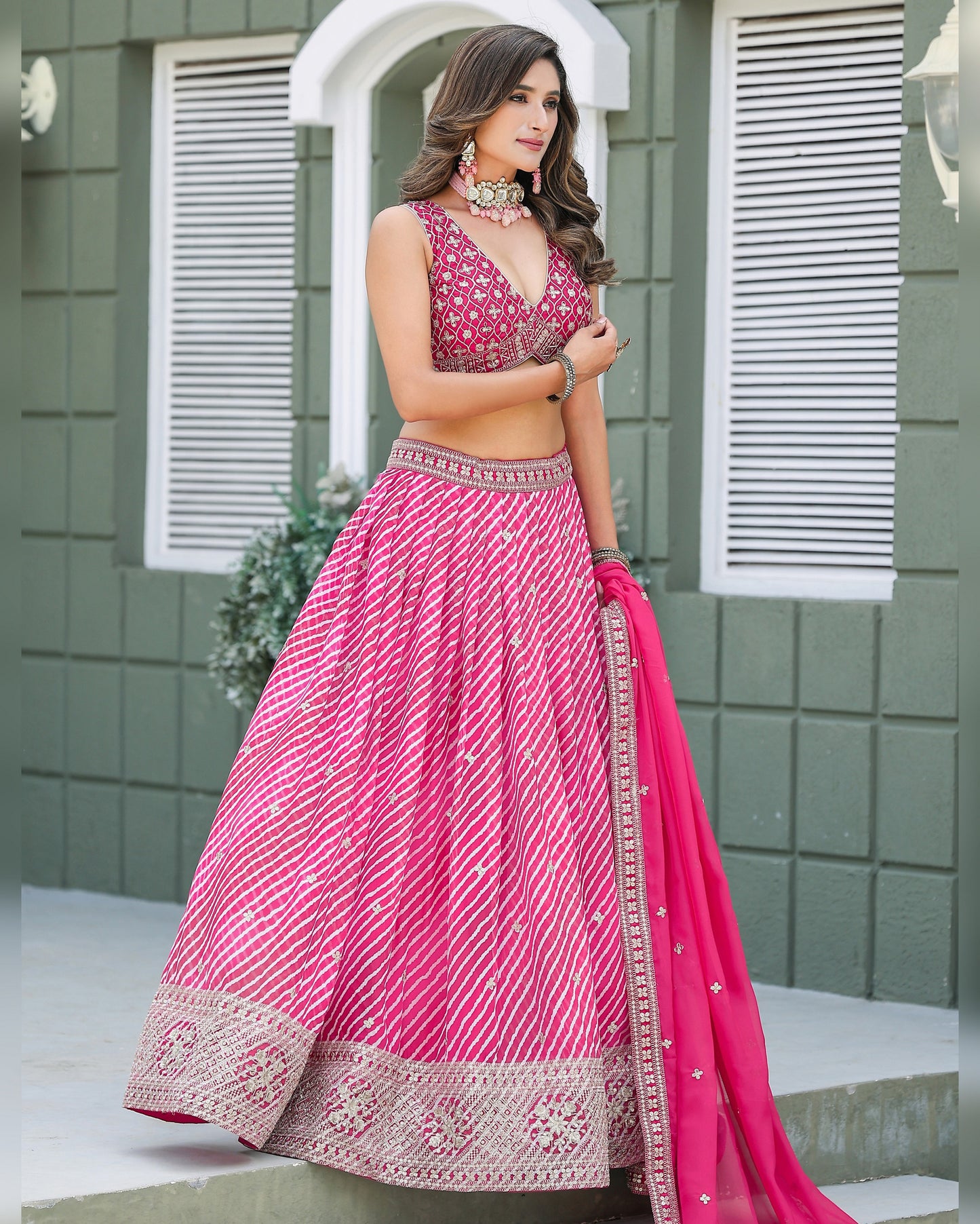 Woman in a pink traditional outfit standing in front of a green wall.