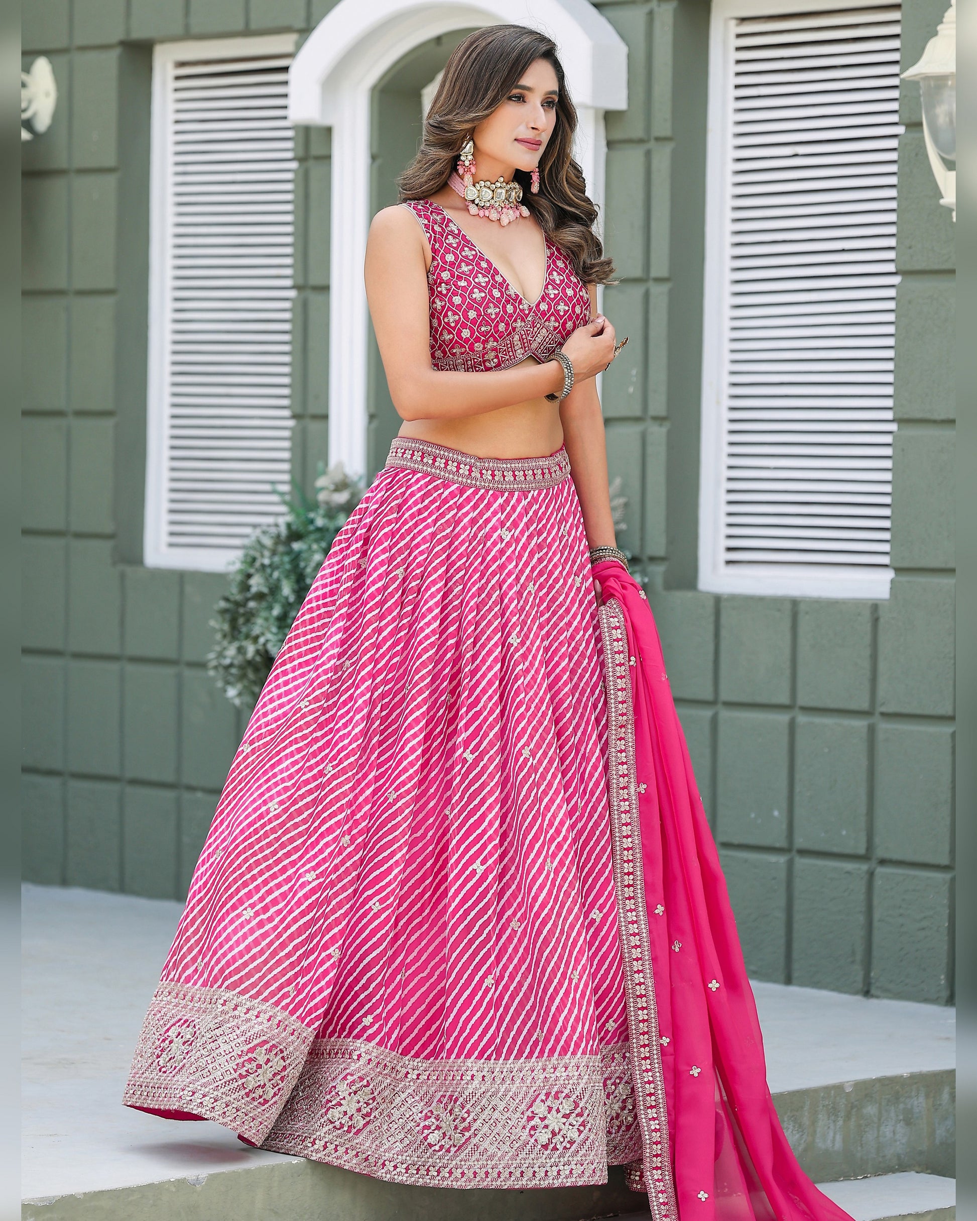 Woman in a pink traditional outfit standing in front of a green wall.