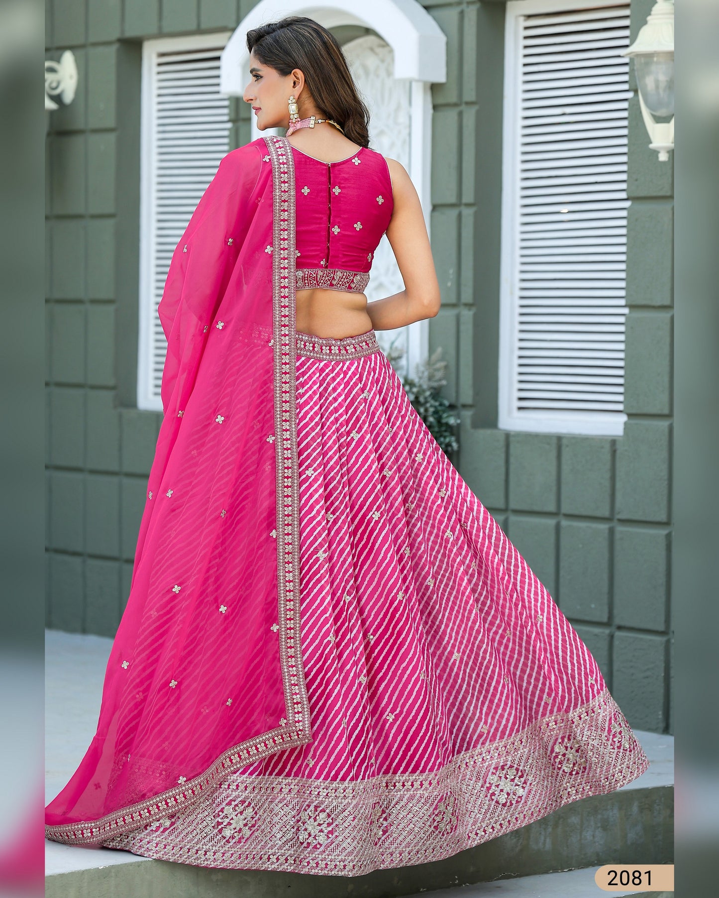 Woman in a pink traditional outfit with intricate designs standing against a gray wall.