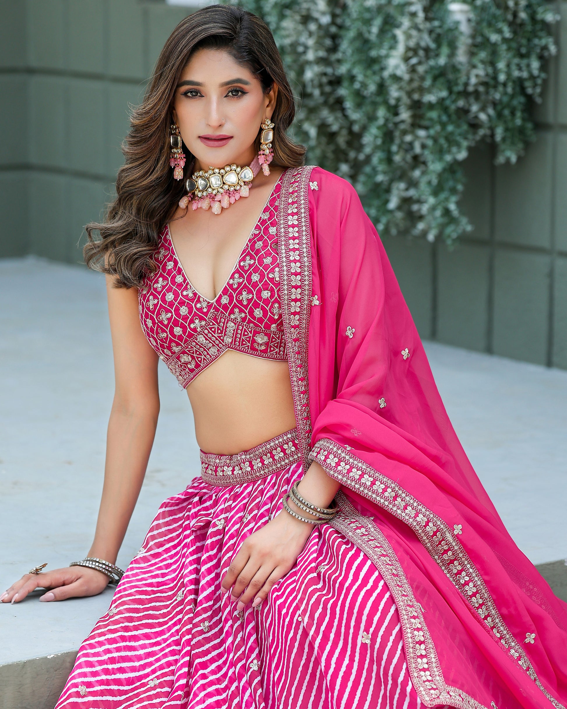Woman in a pink traditional outfit with intricate designs, sitting outdoors.