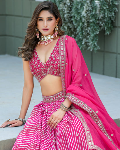 Woman in a pink traditional outfit with intricate designs, sitting outdoors.