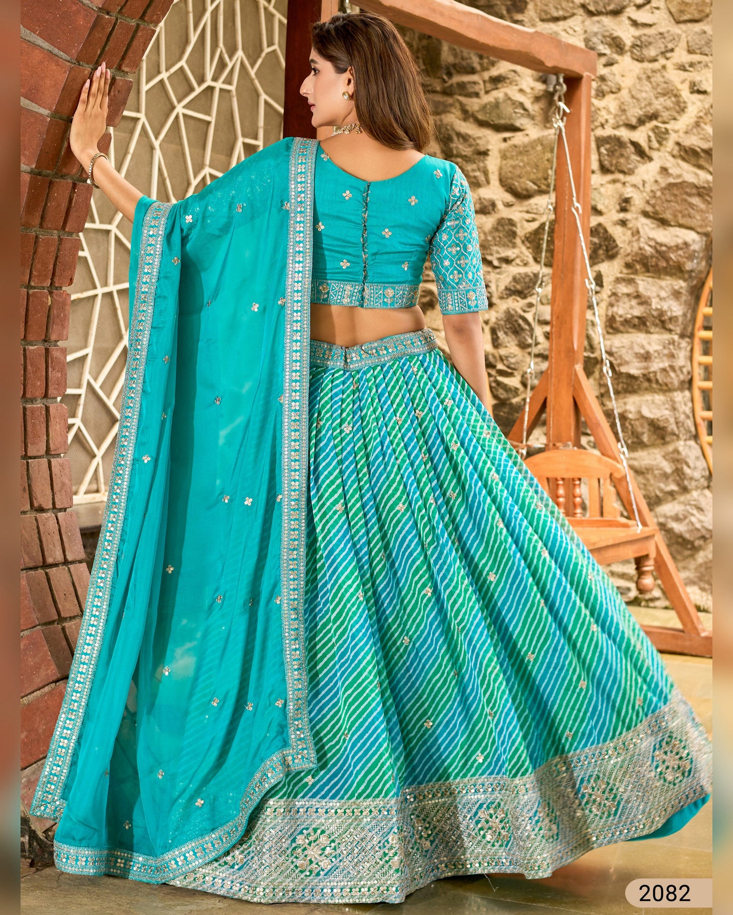 Woman wearing a turquoise traditional outfit with a stone wall and wooden swing in the background