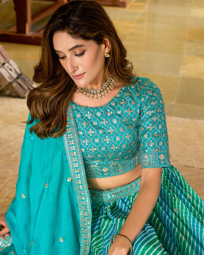 Woman wearing a traditional turquoise embroidered outfit with a matching dupatta.