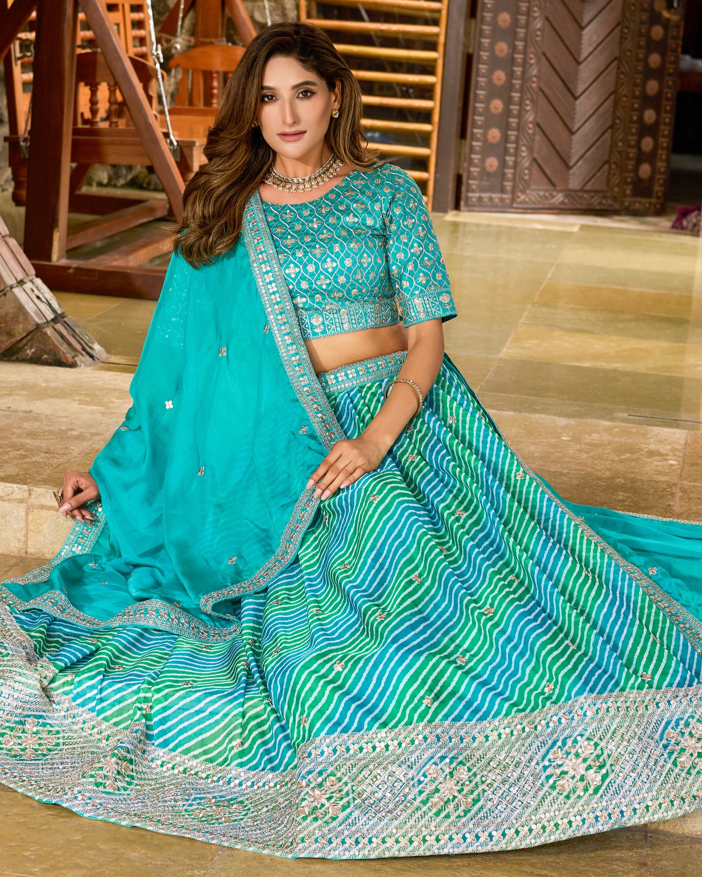 Woman wearing a traditional turquoise and green saree with a matching blouse in an indoor setting.