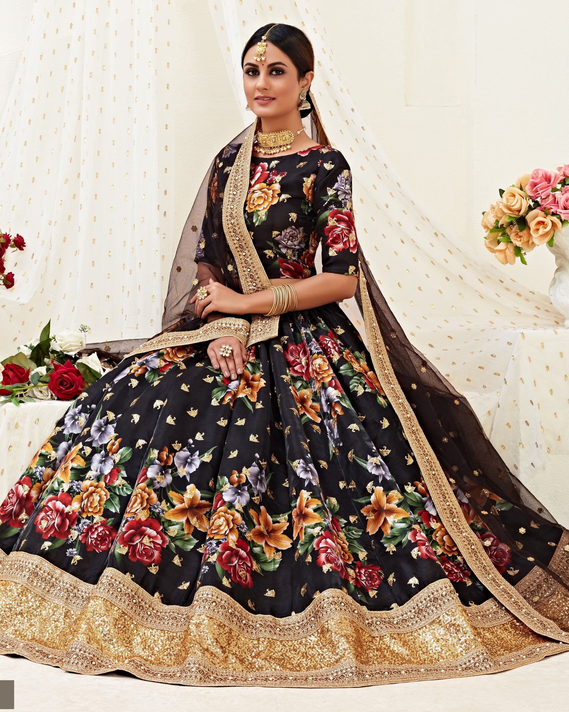 Woman wearing a black floral lehenga with gold border against a white background