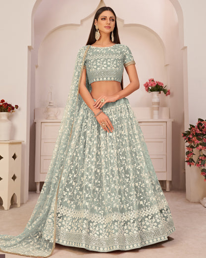 Woman wearing a light green traditional outfit with floral patterns in a decorated room.