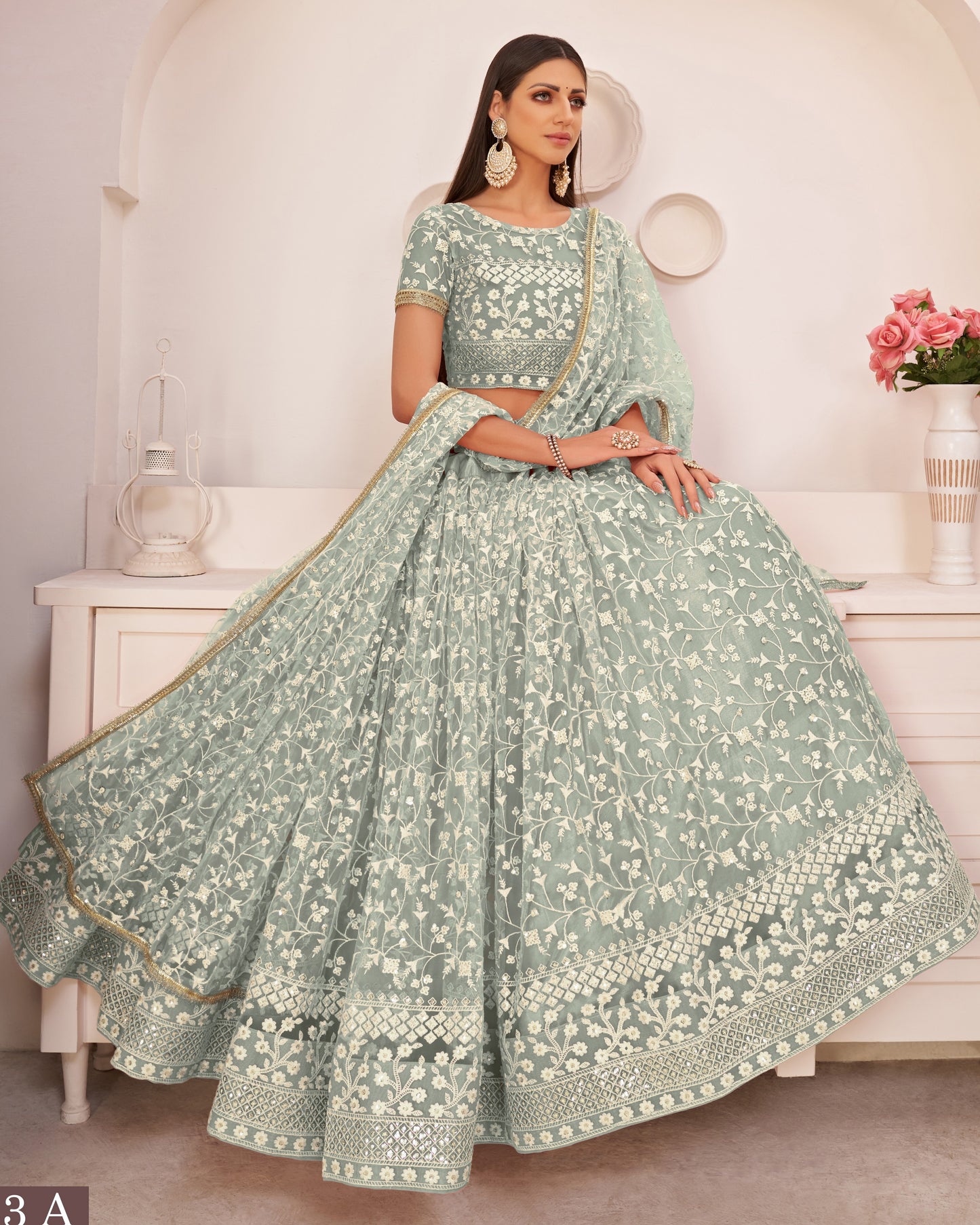 Woman in a light green traditional outfit with floral patterns in a minimalistic room.