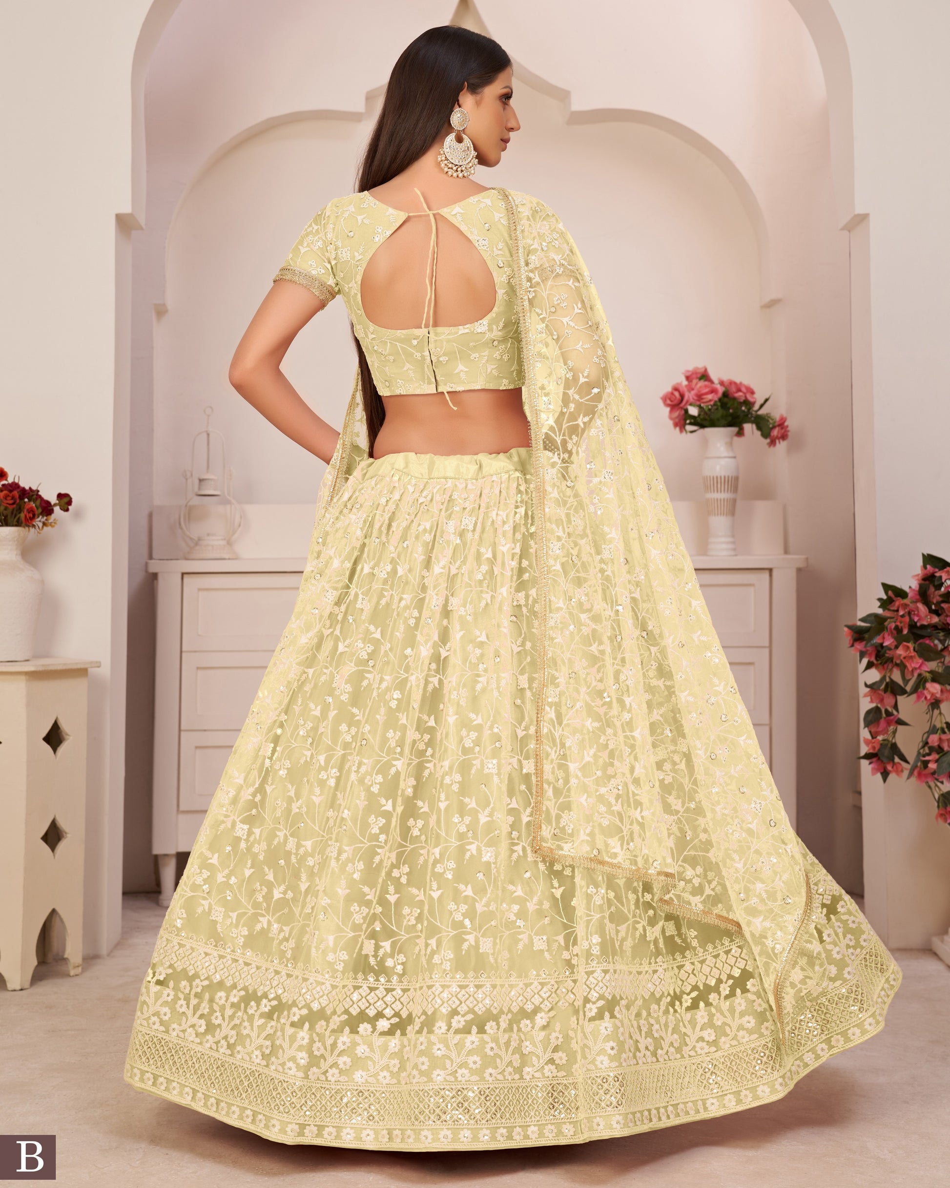 Woman wearing a light green embroidered lehenga in a decorated room.