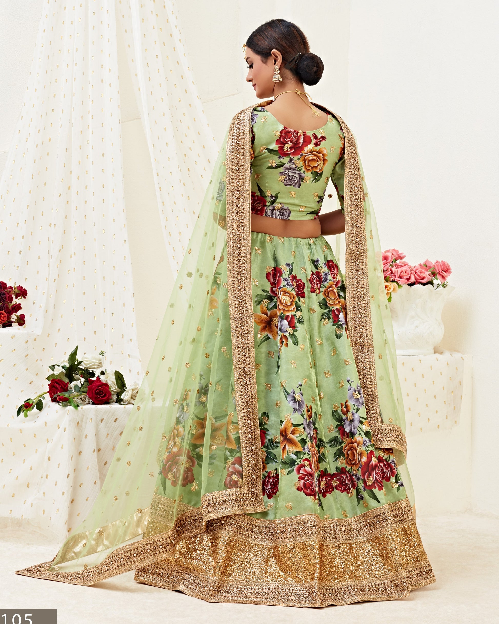 Woman wearing a floral green lehenga with a beige dupatta against a white curtain background