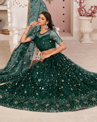 Woman in a green embroidered saree sitting on a white chair in a decorated room.