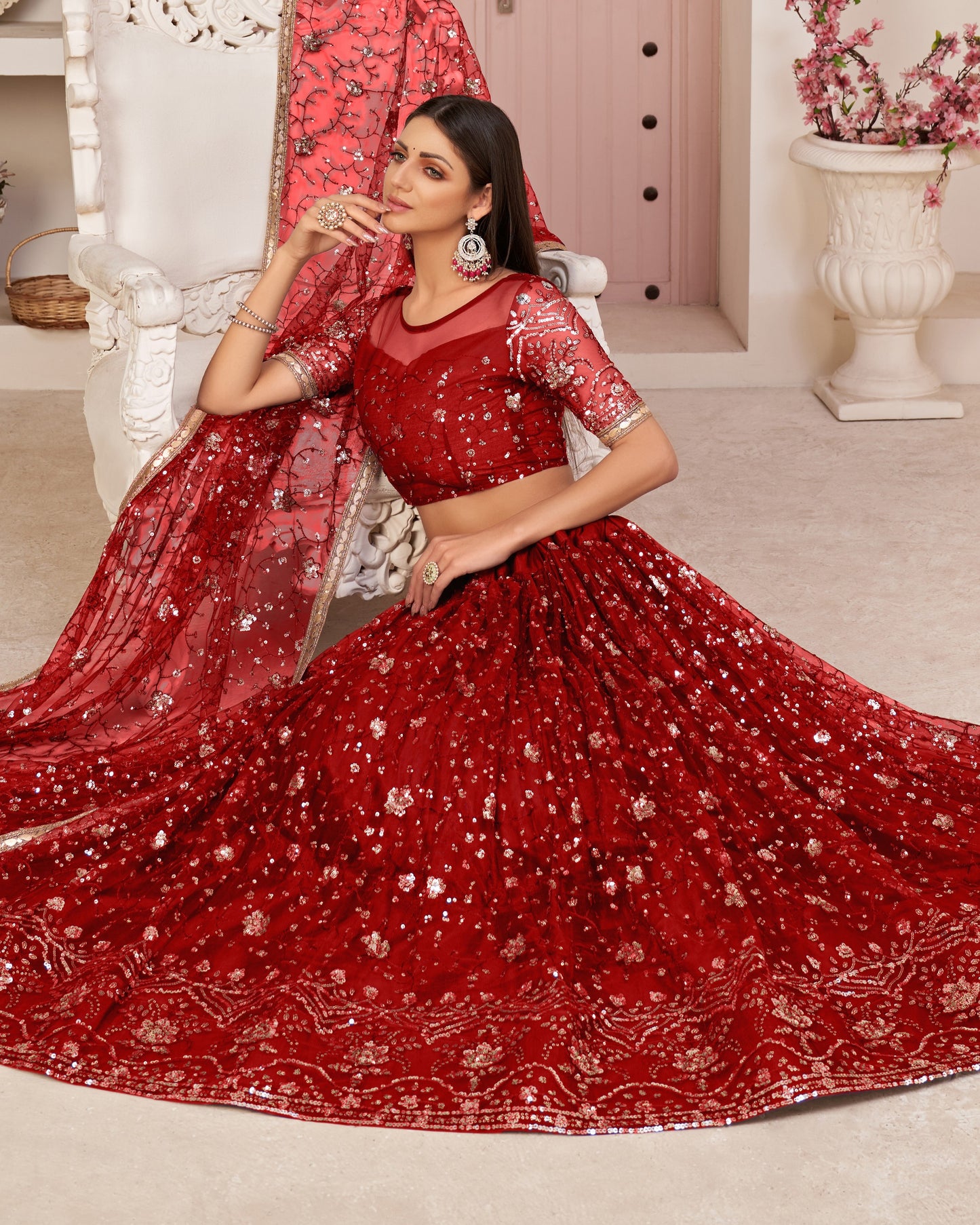 Woman in a red embroidered traditional outfit sitting on a white chair.