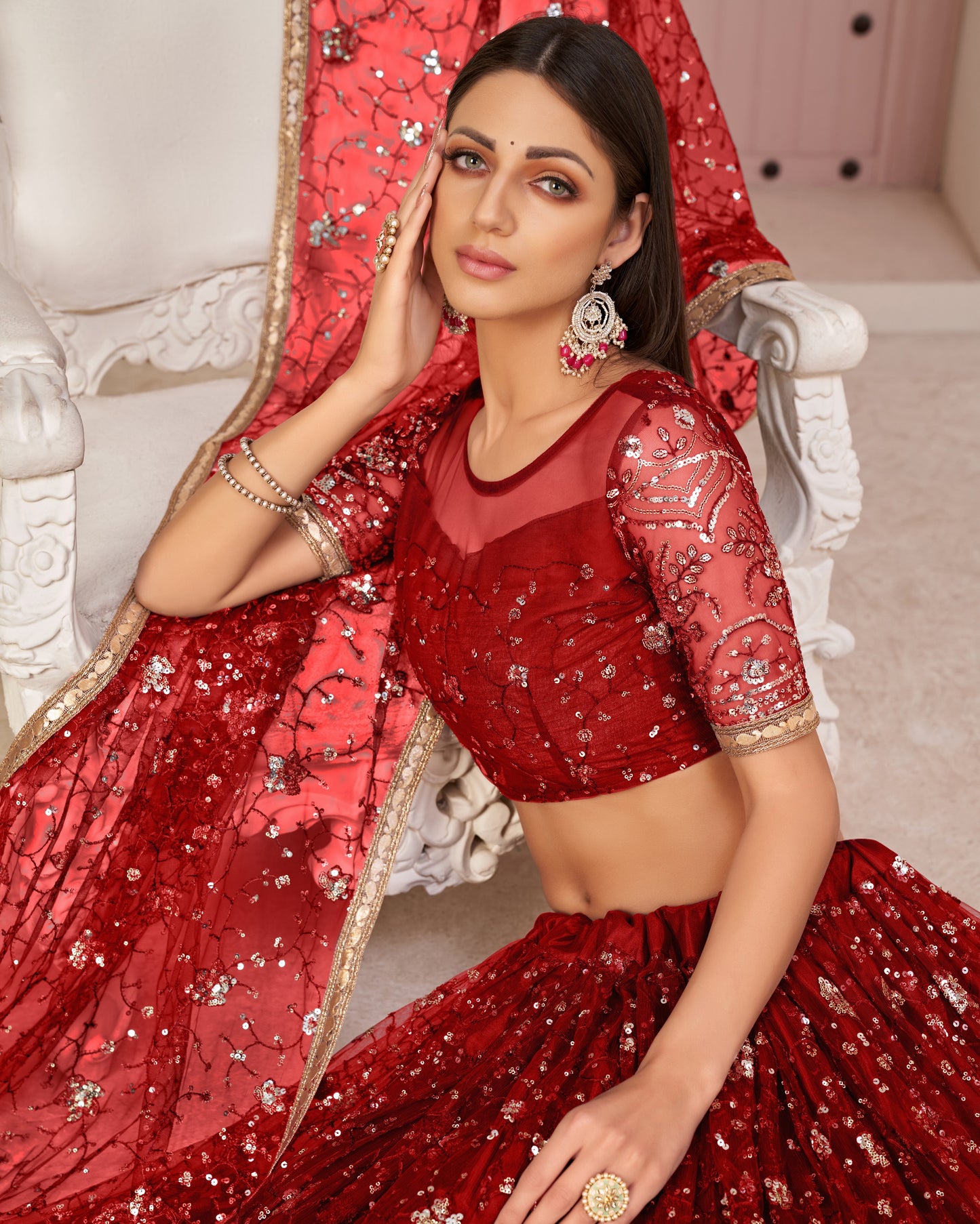 Woman in a red traditional outfit with sequins sitting on a decorative chair.