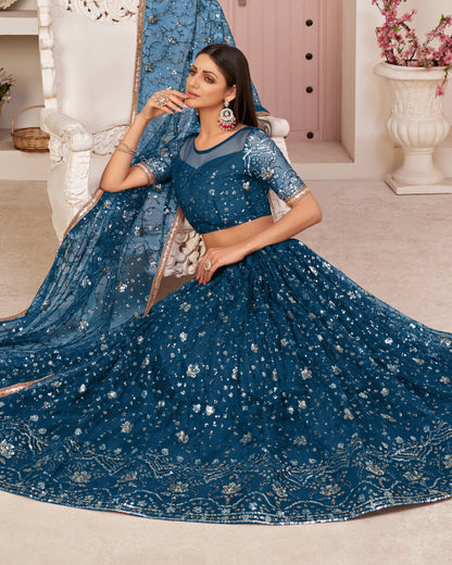 Woman in a blue embroidered saree sitting on a white chair in a decorated room.