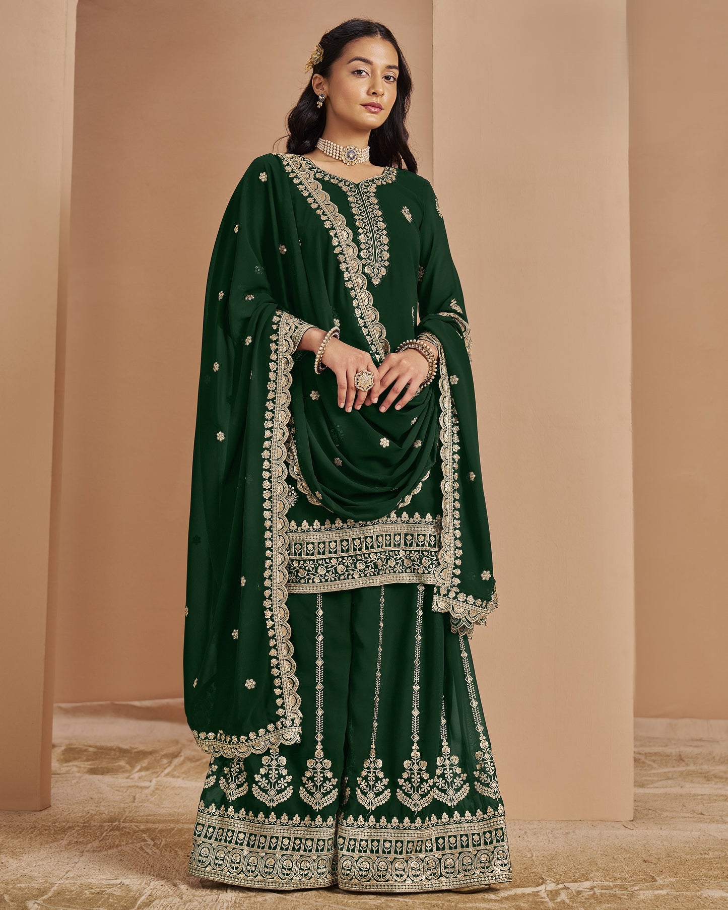 Woman wearing a dark green traditional outfit with intricate embroidery against a beige background