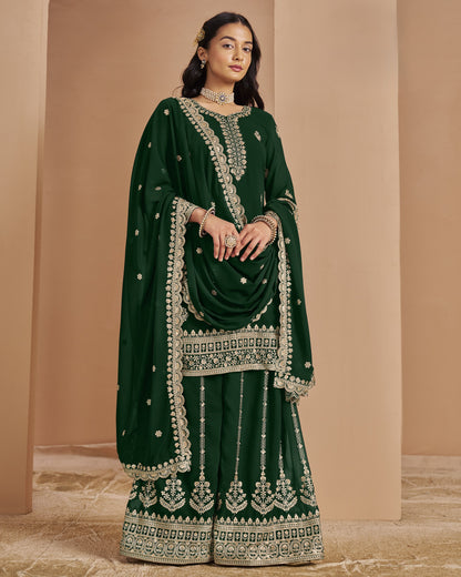 Woman wearing a dark green traditional outfit with intricate embroidery against a beige background