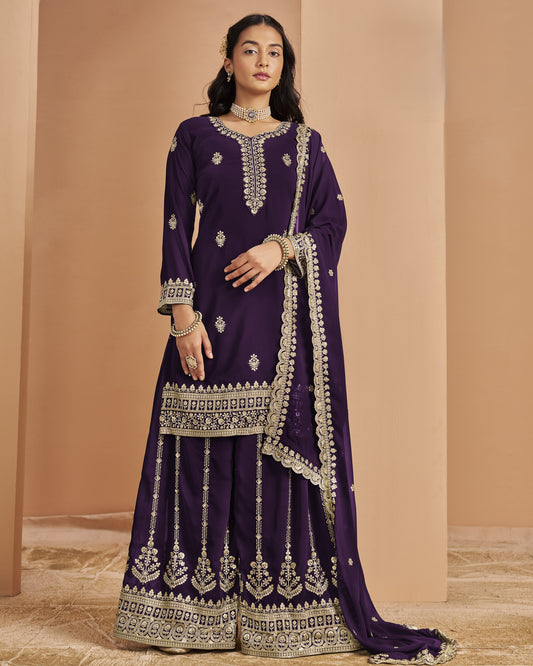 Woman wearing a traditional purple outfit with intricate white embroidery against a beige background