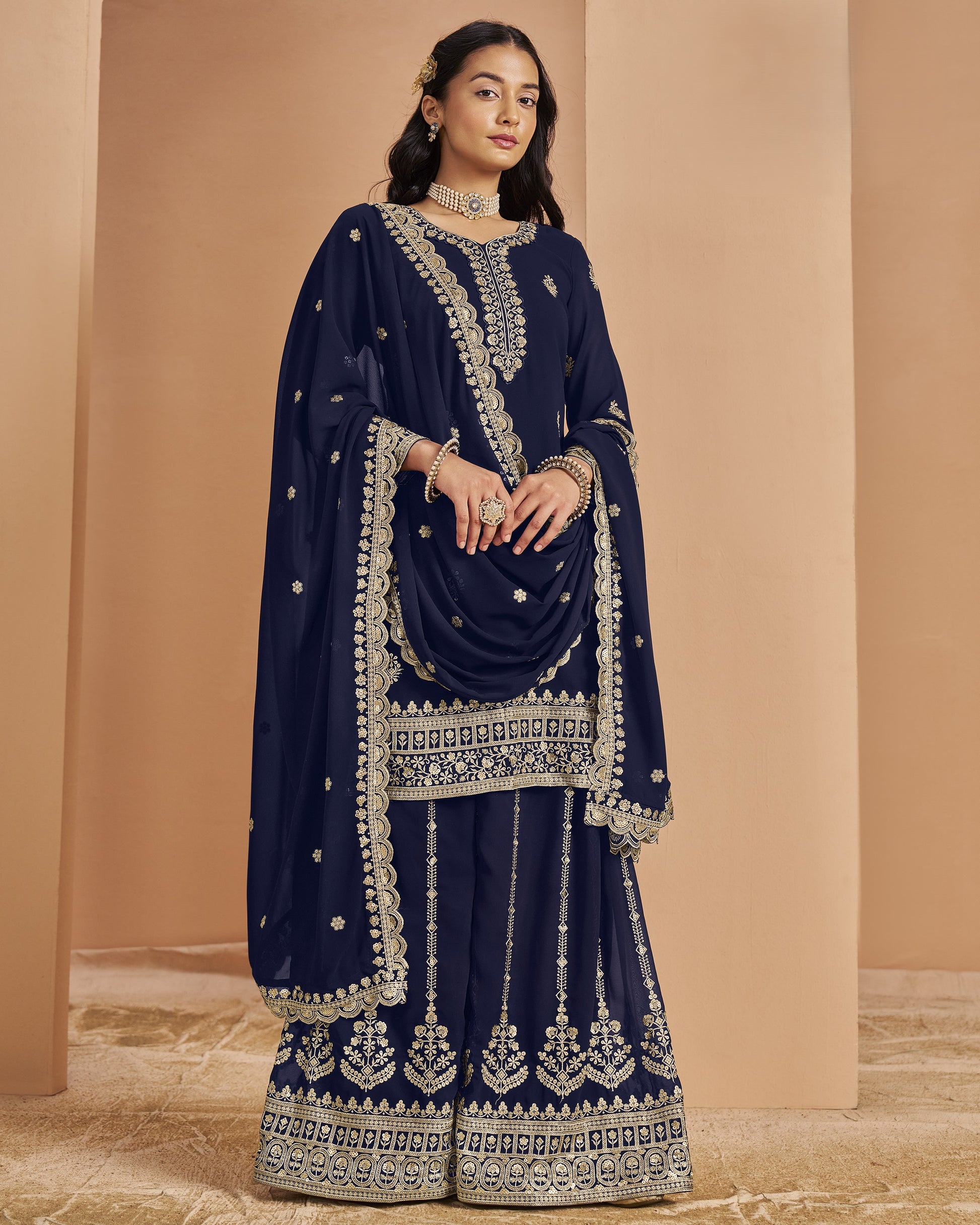 Woman wearing a navy blue embroidered traditional outfit against a beige background