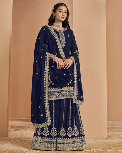 Woman wearing a navy blue embroidered traditional outfit against a beige background