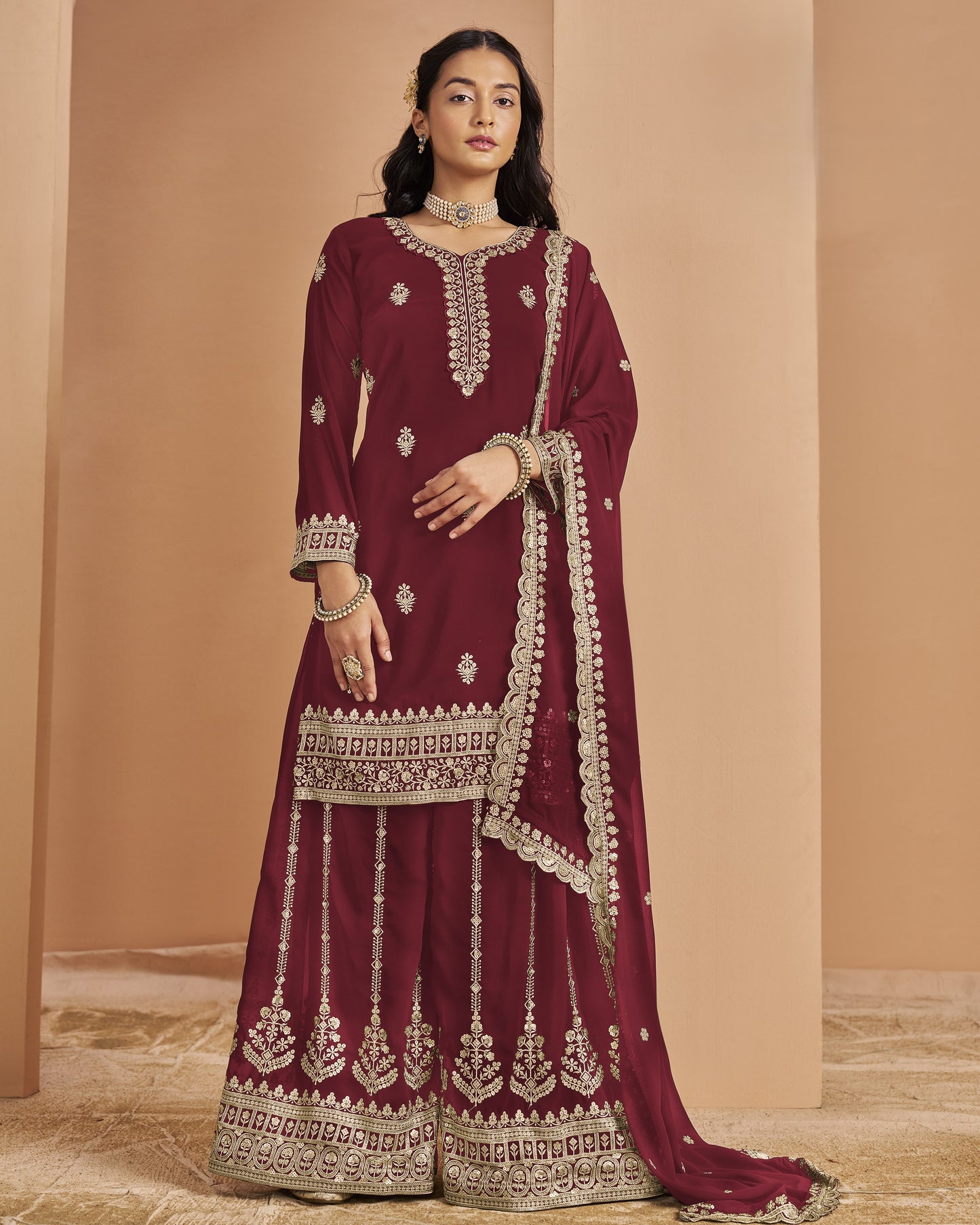Woman wearing a maroon traditional outfit with intricate white embroidery against a beige background