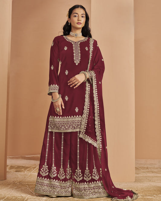 Woman wearing a maroon traditional outfit with intricate white embroidery against a beige background
