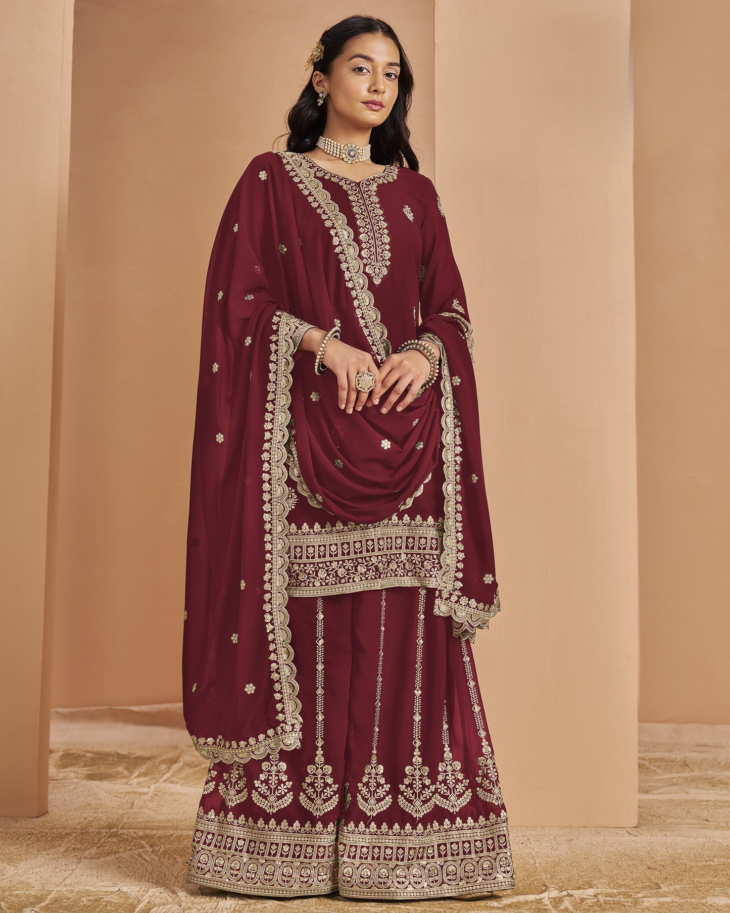 Maroon traditional outfit with gold embroidery on a beige background