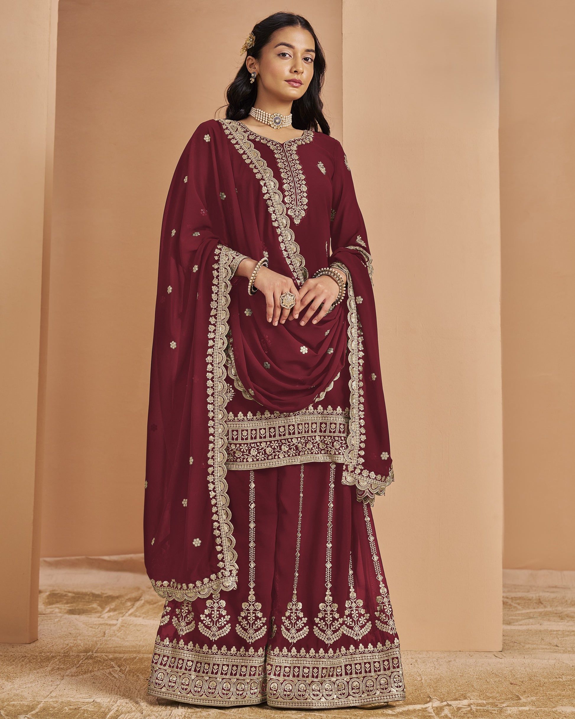 Maroon traditional outfit with gold embroidery on a beige background
