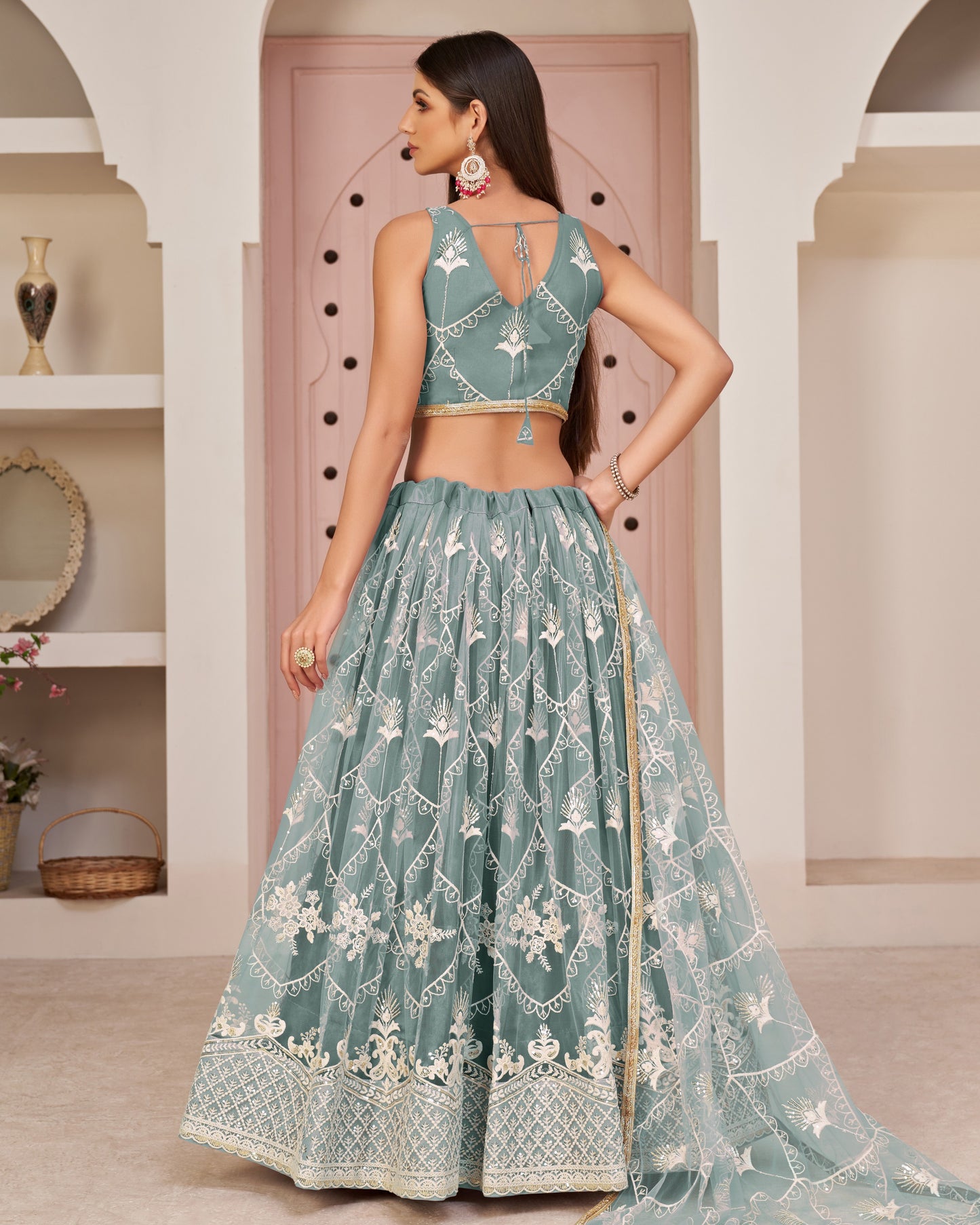 Woman wearing a teal embroidered traditional outfit in an indoor setting.