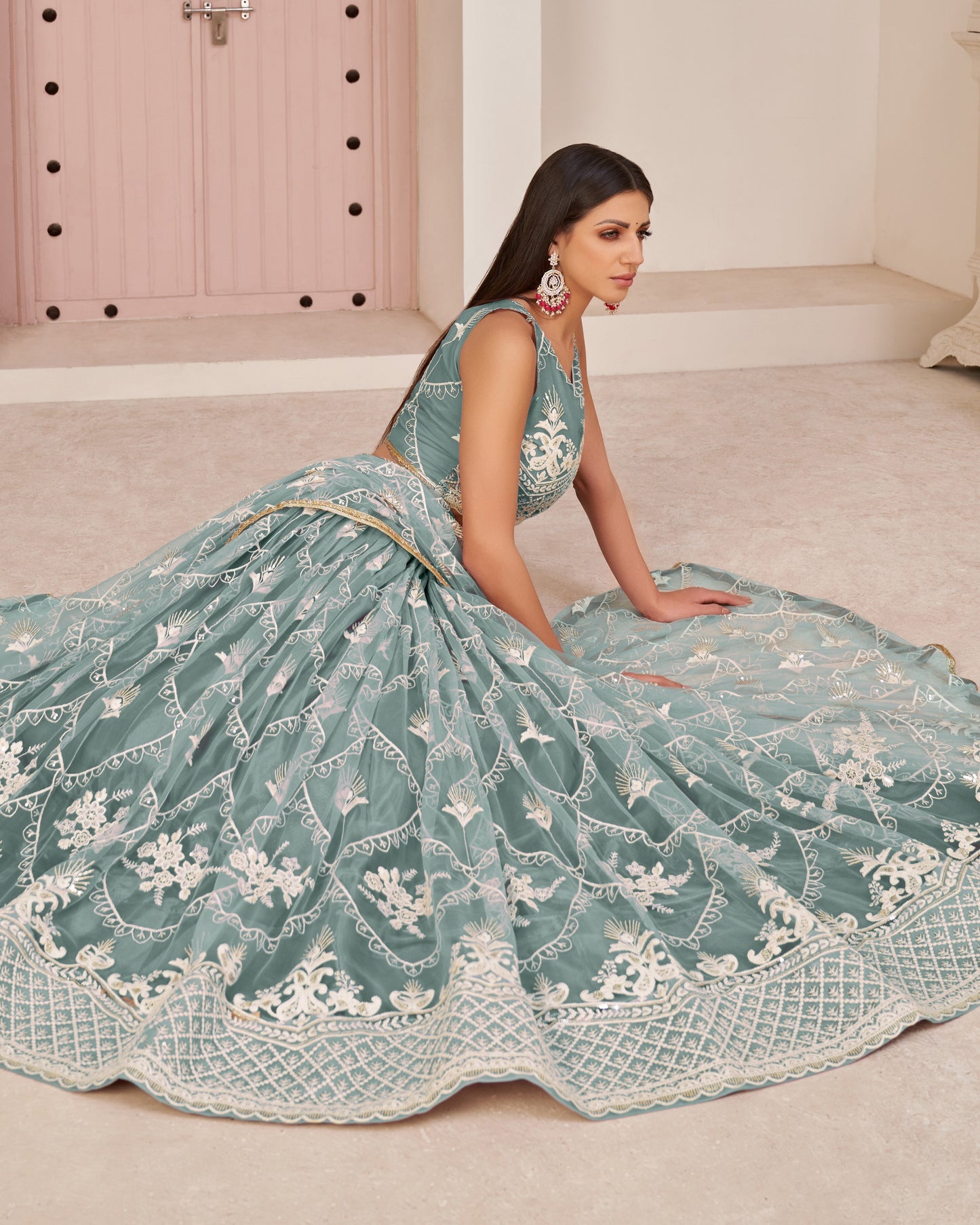 Woman in a light blue embroidered traditional outfit sitting on a beige floor.