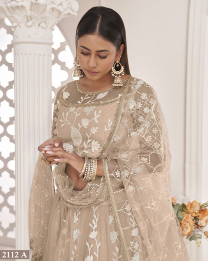 Woman wearing a beige embroidered traditional outfit with floral patterns, standing against a decorative white wall.