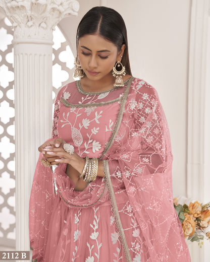 Woman wearing a pink embroidered traditional outfit with floral patterns, standing against a white decorative wall.