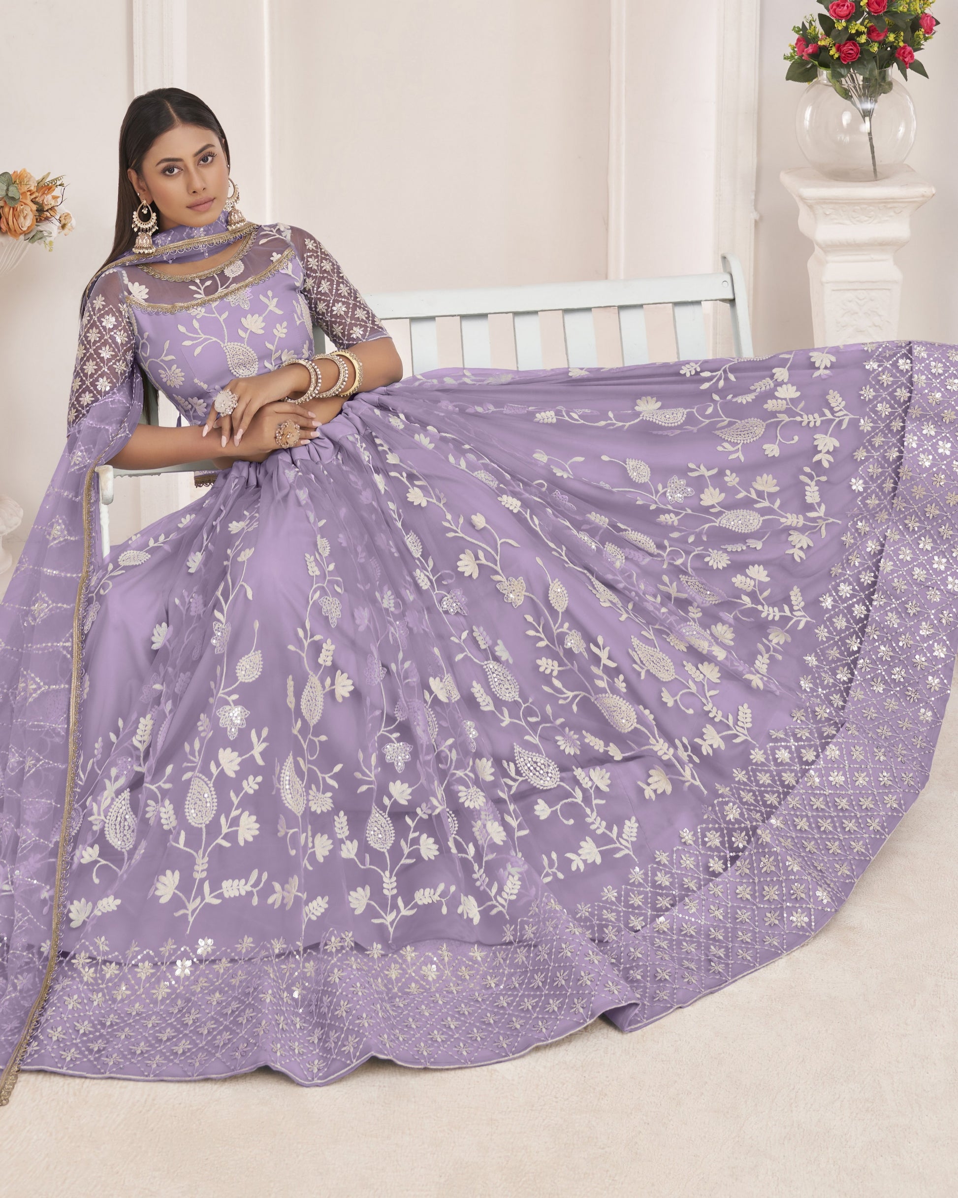 Woman wearing a purple saree with white floral patterns in a well-lit room.
