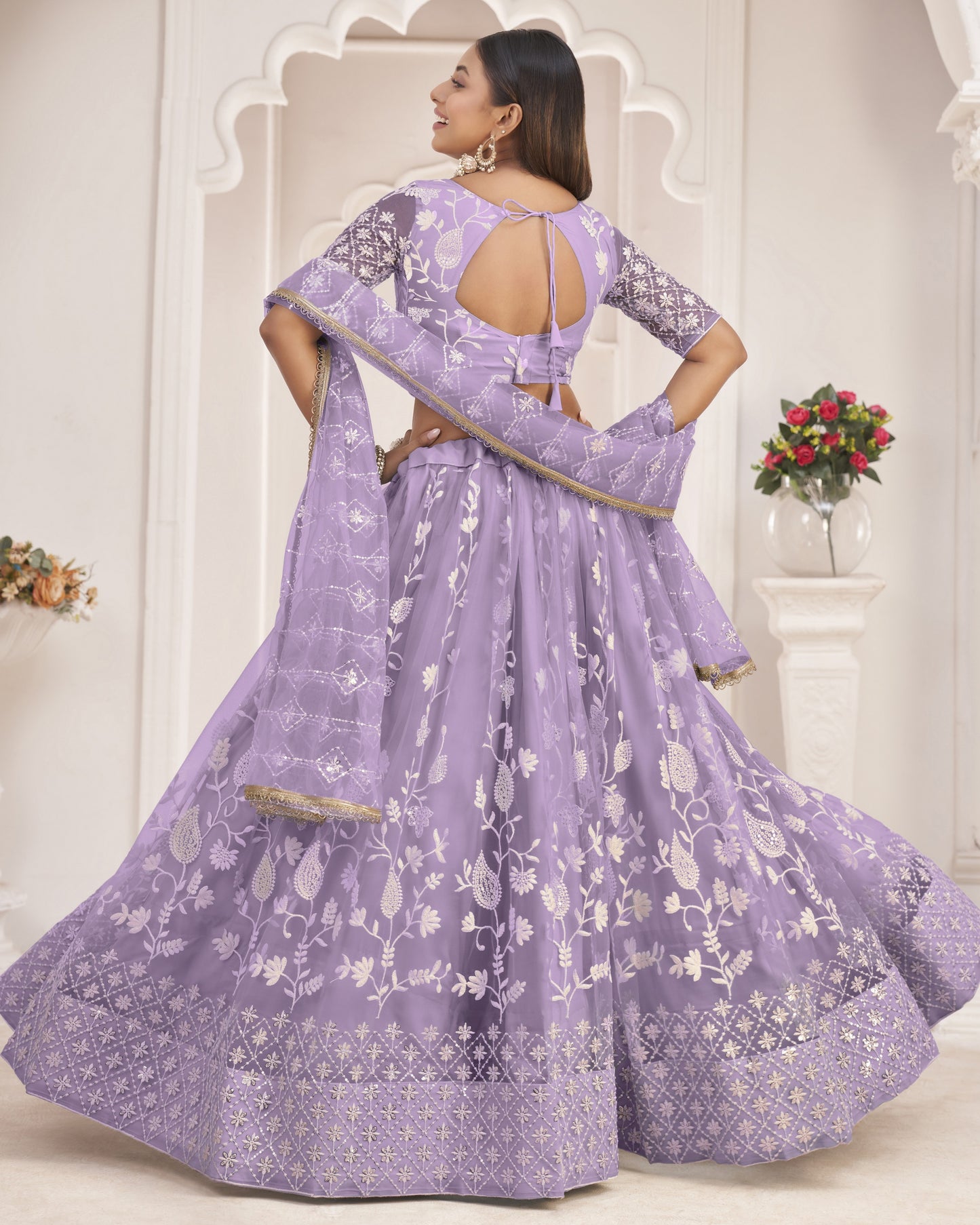 Woman wearing a lavender traditional outfit with floral patterns in a decorated room.