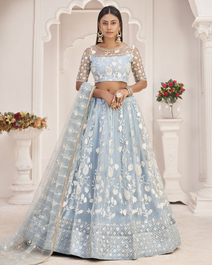 Woman wearing a light blue embroidered traditional outfit in a decorative setting.