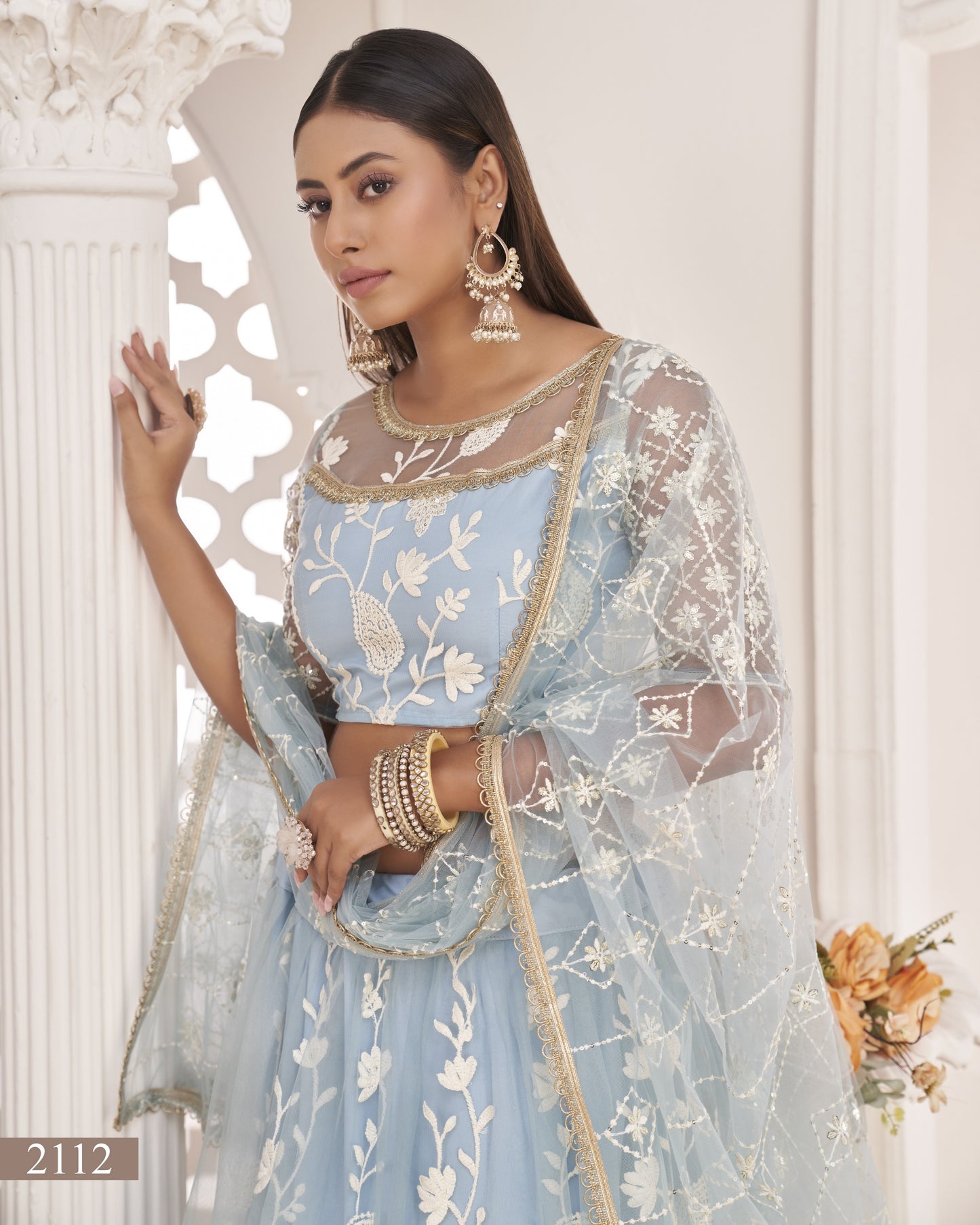 Woman wearing a light blue embroidered traditional outfit with gold accents indoors.