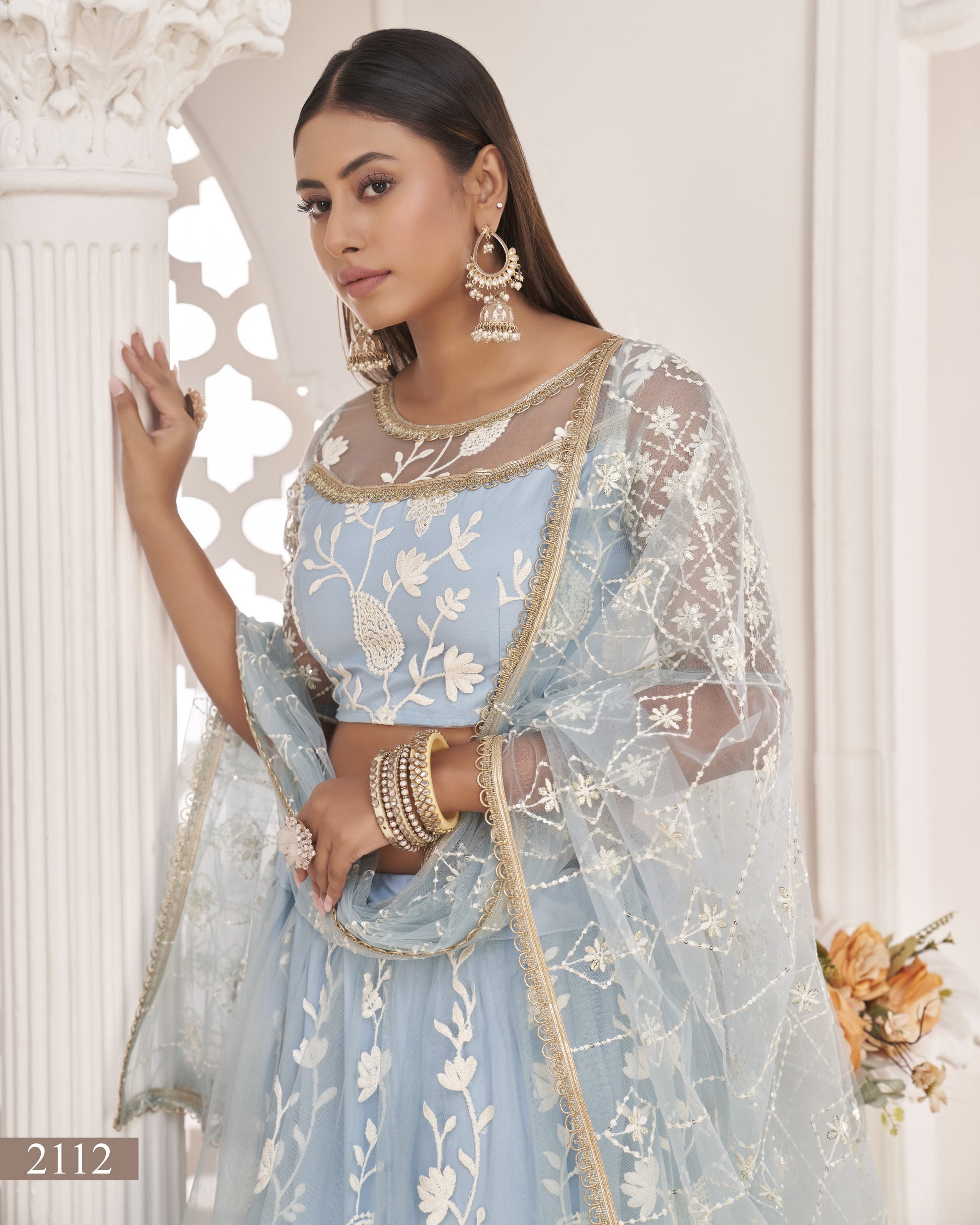 Woman wearing a light blue embroidered traditional outfit with gold accents indoors.