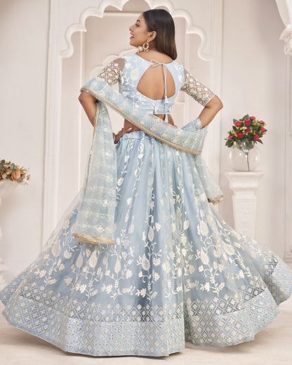 Woman in a light blue embroidered traditional outfit standing in a decorative setting.