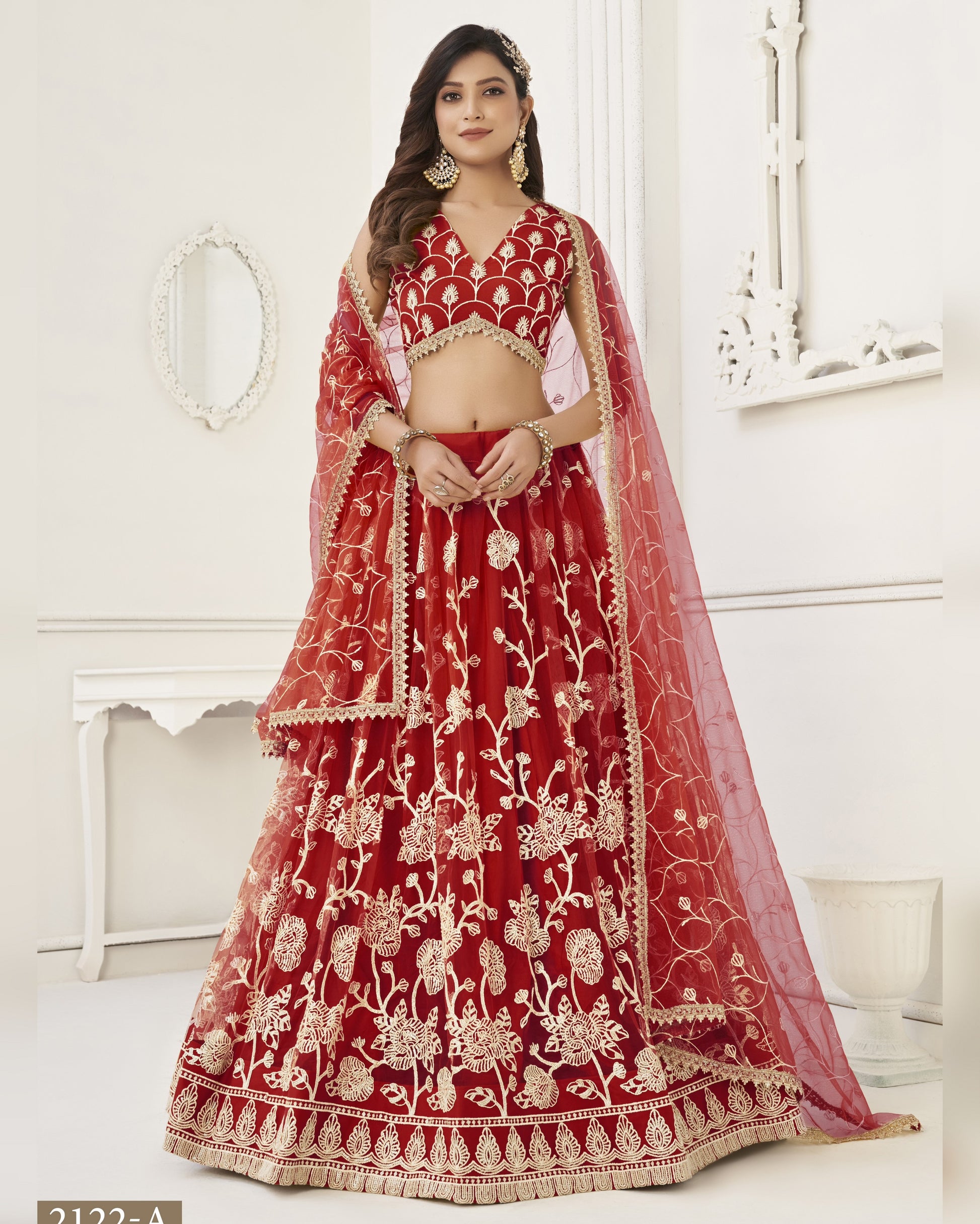Red embroidered lehenga with white patterns worn by a model in a white room.